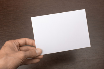 Blank postcard in hand on wooden background. Leaflet A6 mockup