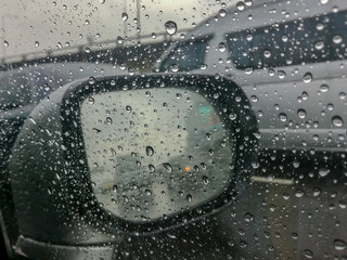 Road view through front car window mirror with rain drops.