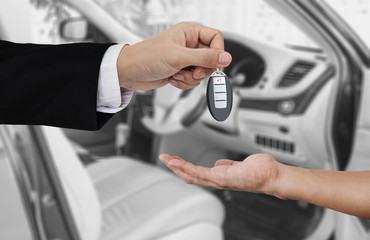 Hand holding car key remote, with modern car backgrounds