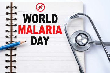 Stethoscope on notebook and pencil with WORLD MALARIA DAY words as medical concept.