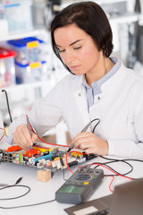 Fototapeta premium Female laboratory assistant Repairs PCB module for CNC robotics. Measurement of the parameters of the electronic system in the laboratory
