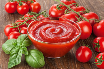 Bowl with ketchup basil and tomatoes on a wooden background.