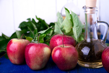 Apple cider vinegar. One glass bottle on blue background. Red apples.