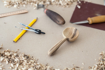 Walnut spoon with carving instruments on kraft paper texture with wooden shavings