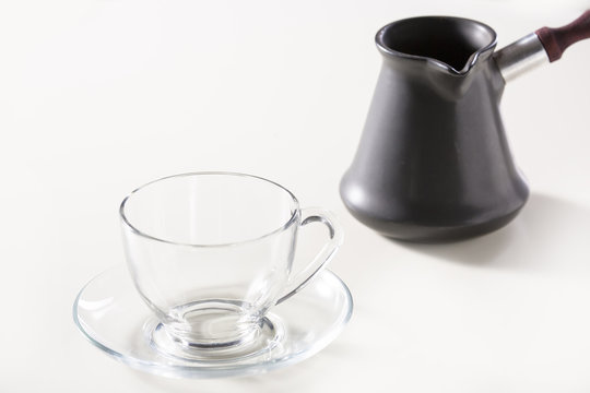 Transparent cup and turk for coffee on a white table.