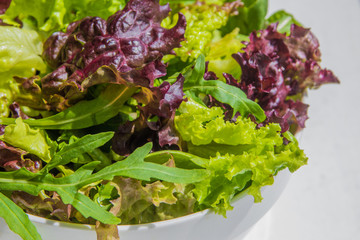 Salad leaves, purple lettuce, spinach, arugula. Mixed fresh salad in a white bowl