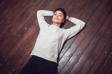 Attractive brunette in a gray sweatshirt lies on a wooden floor. Mock-up.