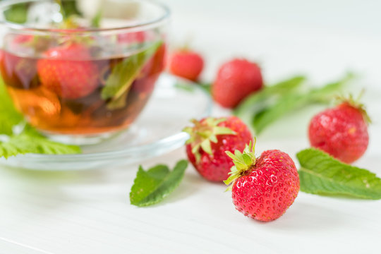 Fresh strawberry. Glass cup of summer tea with fresh strawberry. Green leaves. Fresh mint. White wooden table. Shallow depth of field.