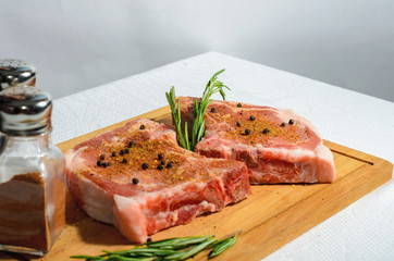 Two appetizing pieces, pork entrecote on a wooden cutting board with salt shaker and pepper and rosemary