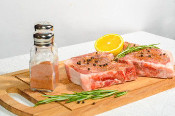 Two appetizing pieces, pork entrecote on a wooden cutting board with salt shaker and pepper and rosemary and lemon
