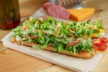 Healthy fresh crusty baguette submarine sandwich with salami, cheese and rucola. Selective focus