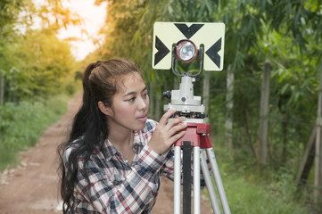 Female Surveyor or Engineer making measure by prism reflector on the street in a field.