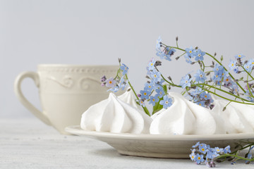 White marshmallows and lilac forget-me-not flowers with green leaves on a white background.