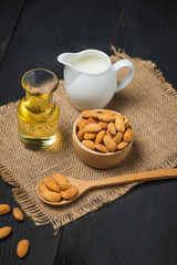 Almond oil in bottle and milk with almonds on black wooden table