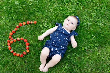 Adorable baby girl on grass with strawberries six moths © Irina Schmidt