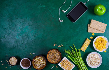 Apple,asparagus,bean sprouts,wheat germ,peas,chia seeds,oatmeal, smartphone on green background. Top view diet concept background