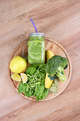 Fresh green vegetables and green smoothie in jar. Detox, diet or healthy food concept. Mason jar of dietary drink with broccoli, spinach, microgreens, lime and banana on wooden background. Top view.