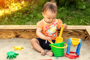 Happy little girl playing in a sandbox on the playground. Summertime children activities