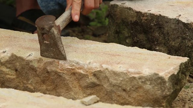 A stonecutter or stonemason is profiling the cut of a stone with a wide chisel. He is cutting the stone in a traditional way, manually. Closeup.