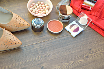 Beige leather spring female shoes, red jeans, cosmetics (mascara, lacquer, eye shadow, rouge, perfume, lip gloss) on a wooden background