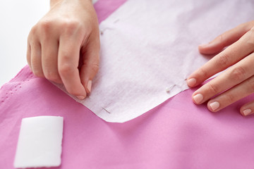 woman with pins stitching paper pattern to fabric