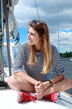 Smiling girl sitting on yacht deck. Attractive girl on a yacht at summer day