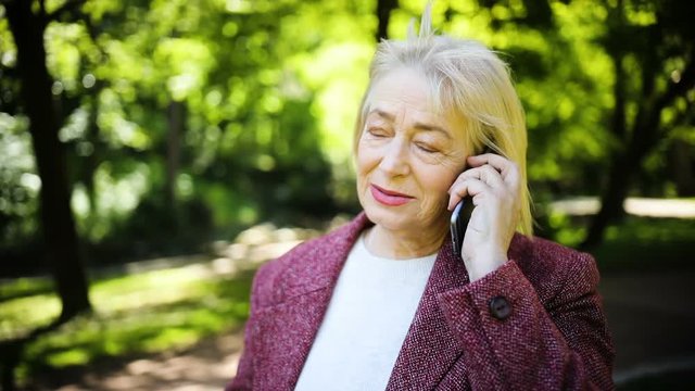 Beautiful older woman speaks on the phone outdoors in the sunlight