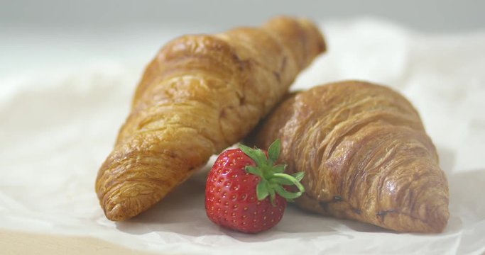 Close-up shot of baked croissant with one fresh strawberry on plate. 