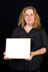 Naklejka premium Beautiful light overweighted european red haired adult carrying a white blank board in front of a black background - studio shot