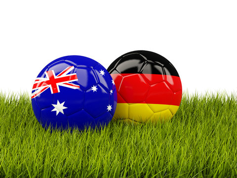 Two footballs with flags of Australia and Germany on green grass