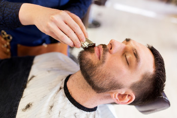 Obraz na płótnie Canvas man and barber with trimmer cutting beard at salon