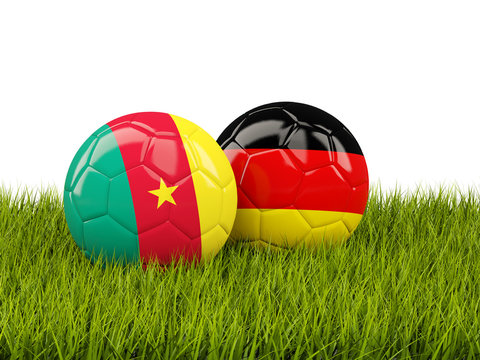 Two footballs with flags of Cameroon and Germany on green grass