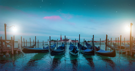 Fototapeta na wymiar Mystical landscape with gondolas on the Grand Canal on the background of Church of San Giorgio Maggiore at dawn in the light of lanterns and stars in Venice, Italy, Europe.