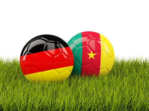Two footballs with flags of Germany and Cameroon on green grass