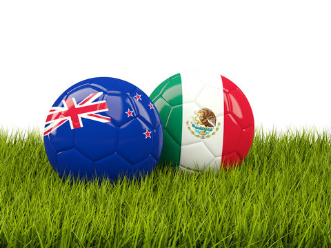 Two footballs with flags of New Zealand and Mexico on green grass