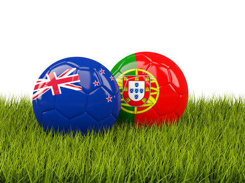 Two footballs with flags of New Zealand and Portugal on green grass