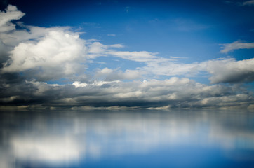 Blue sky. Dramatic clouds over sea. Blurred reflection of sky in water
