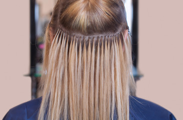The hairdresser does hair extensions to a young girl, a blonde in a beauty salon. Professional hair care.