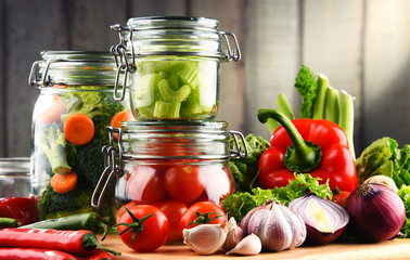 Jars with marinated food and raw vegetables on cutting board