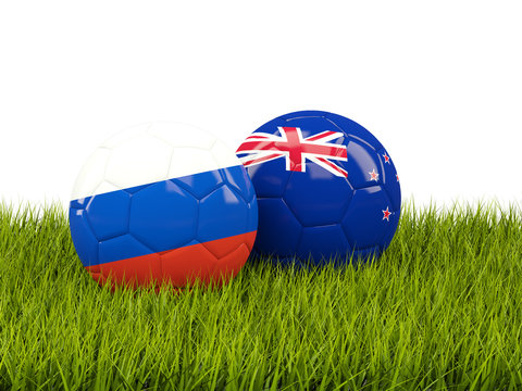 Two footballs with flags of Russia and New Zealand on green grass