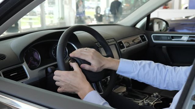 men holds steering wheel inside car, man's hands at helm, fortunate buying automobile, enjoying good purchase in car sales center, customer delight on auto, male buy new vehicle, new machine showroom