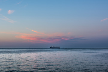 Fototapeta na wymiar Big ship standing on the horizon under pink sunset cloud. Roadstead of Gdansk port.