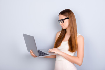 Success and work, study concept. Young serious lady journalist is working on her laptop, wearing casual clothes and glasses, on pure light background