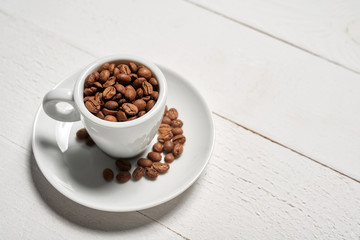 Coffee cup full of coffee beans on white rustic wooden background