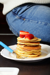 Pancakes with red strawberries in plate on kitchen table, near woman leg