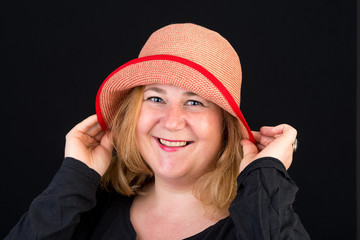 Portrait of a happy attractive european light overweighted red haired female posing with a red hat - studio shot on black background