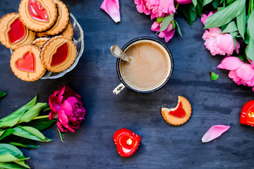 The concept of morning coffee in a romantic style on the black wooden background. Peonies flowers and petals, cookies, heart candles, mug with coffee . Valentine's love day. Top view.