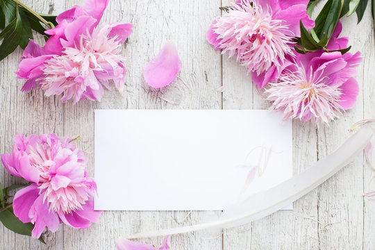 Mockup- flowers, peonies on a wooden table, white card. Woman's desk.