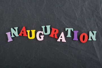 Obraz premium Iinauguration . English word on black board background composed from colorful abc alphabet block wooden letters, copy space for ad text. Learning english concept.