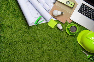 Workplace with helmet, blueprints, laptop and notepad on grass background. Top view with copy space